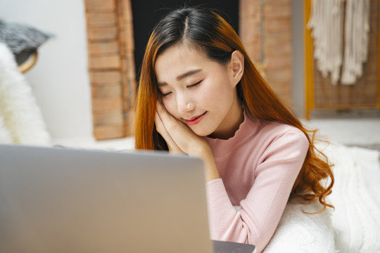 美丽的亚洲年轻女子一边看笔记本电脑一边睡觉。