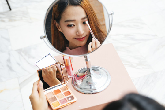 美丽的亚洲女人在化妆时对着镜子画睫毛。