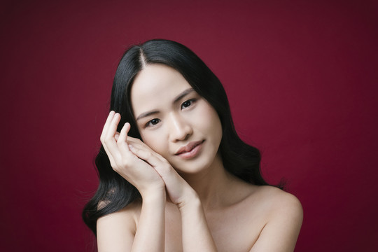 美丽的年轻亚洲女性肖像，皮肤干净完美，自然妆容，红色背景。
