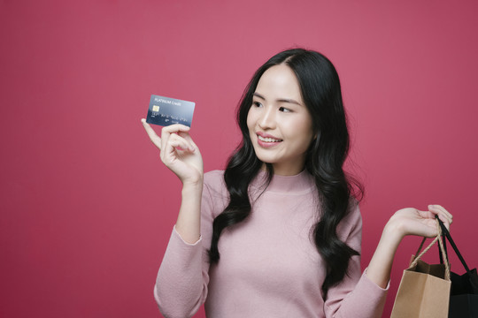 展示信用卡和购物袋的年轻亚洲女性肖像。