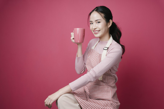 粉红色背景下，年轻的亚洲女性手持咖啡杯的肖像。