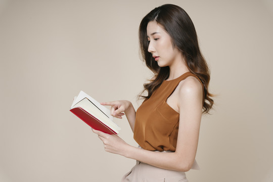 美丽的亚洲年轻女子看书的侧视图。