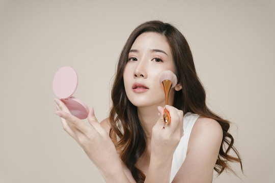 美丽的年轻亚洲女性在脸上涂抹化妆粉的肖像。