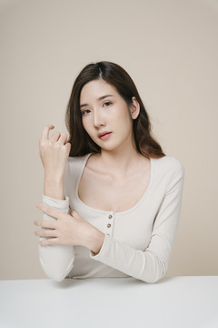 在米色背景下，一位年輕美麗的亞洲女子撫摸手臂的肖像。