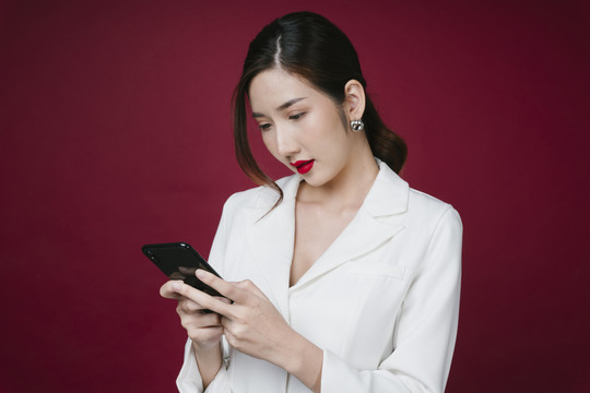 穿着白色夹克套装、使用智能手机进行化妆品购物的亚洲年轻美女肖像。