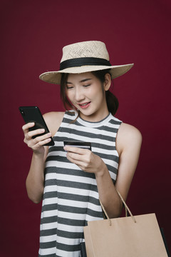 戴着帽子的美丽亚洲年轻女子的肖像，用手机和信用卡进行网上购物。