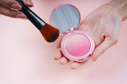 粉红色背景上隔离的化妆刷和腮红盒的特写镜头。