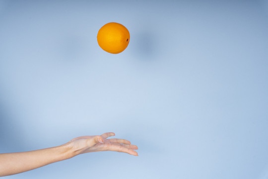 一个女人的手向空中扔了一个橘子，背景是蓝色的。
