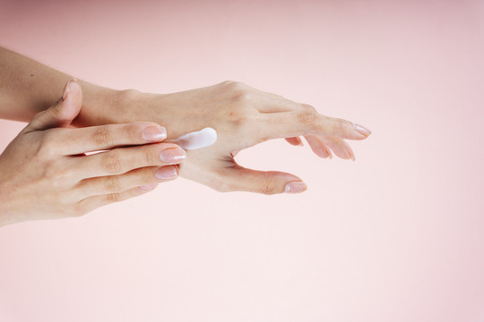 女性手用乳液隔离霜，粉红色背景。