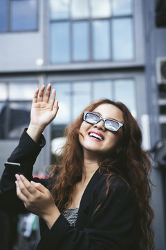 穿着黑色夹克和太阳镜的酷亚洲女商人向朋友挥手致意。