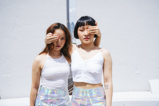 两位亚洲年轻女子用手捂住对方眼睛的肖像。