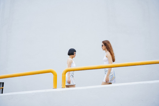 侧视图——两位戴着太阳镜的年轻亚洲女性在城市街道上相互擦肩而过的照片。