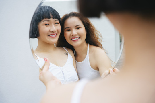 两位快乐的年轻亚洲女性对着镜子微笑的肖像。