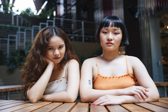 两位年轻的亚洲女性在户外咖啡馆看着摄像机的照片。