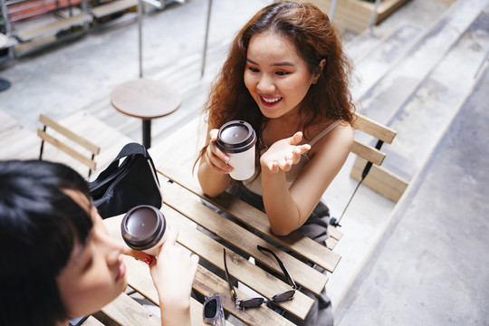 开朗的亚洲年轻女子和朋友在咖啡馆里喝咖啡。