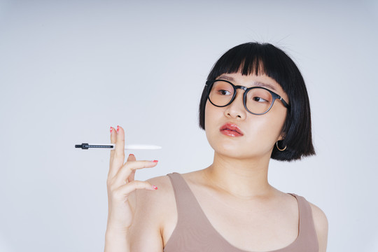 年轻亚洲女性短发的肖像，戴着墨镜，手持钢笔，白色背景。