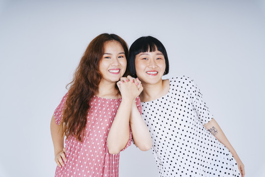 在白色背景上，两位年轻的亚洲女性手牵着手的欢快肖像。