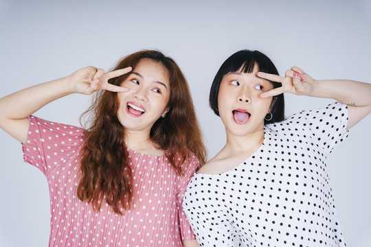 两名年轻亚洲女性的肖像，在白色背景上穿着粉色和白色的帕卡多特隔离服。