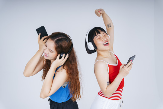 在白色背景下，两位年轻快乐的亚洲女性一边听音乐一边跳舞。