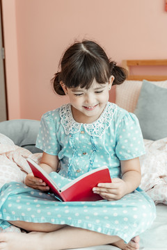 穿着蓝色衣服的快乐女孩在卧室看书。