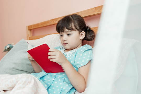穿着蓝色衣服的可爱女孩在卧室睡觉前看书。