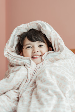 特写肖像——卧室里穿着柔软毯子的可爱女孩。