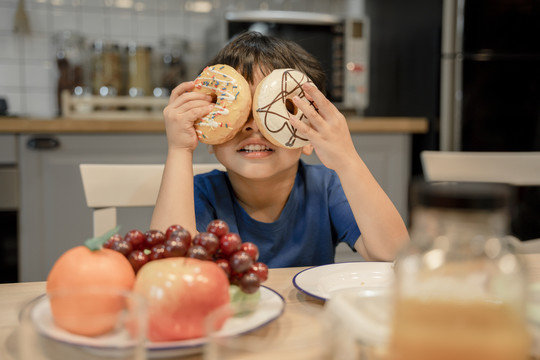 小男孩在厨房里用甜甜圈做有趣的眼镜。