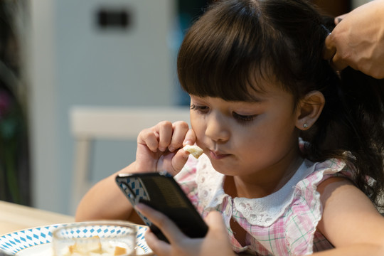 小女孩在家吃早餐和使用智能手机的特写照片。