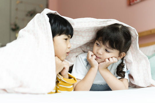 男孩和女孩在卧室的毯子下玩得很开心。