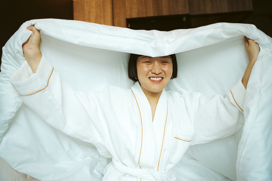 亚洲短发女子在卧室里玩白色毯子。