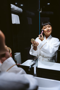 短发亚洲女人用粉刷把镜子前的棍子。