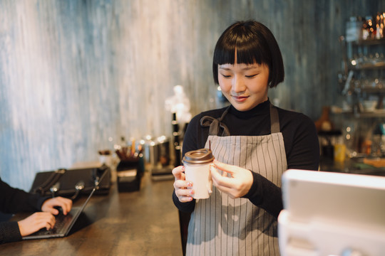 亚洲女咖啡师在咖啡馆为顾客煮热咖啡。