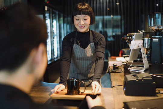 亚洲短发巴蒂斯塔女士，在酒吧为顾客提供热咖啡。