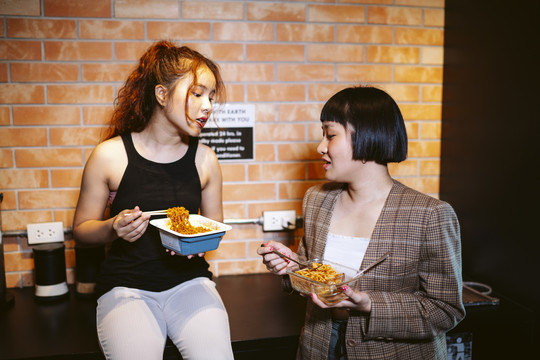 两个亚洲女人在厨房里一起吃辣面条。
