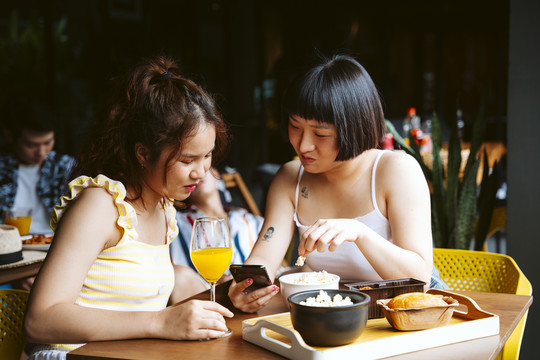 两位年轻的亚洲女性正在看智能手机获取社交媒体新闻。
