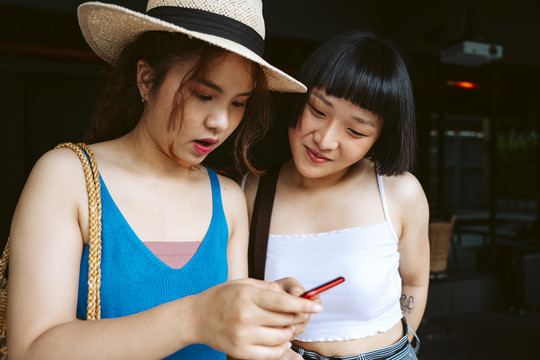 两名亚洲女性好友用智能手机查看旅游目的地。