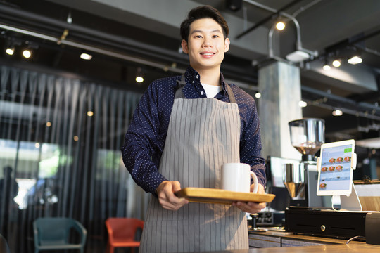 亚洲咖啡师在咖啡馆为顾客提供热咖啡。