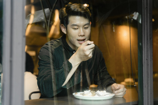一个穿着黑衬衫的亚洲人独自在咖啡馆吃午饭。