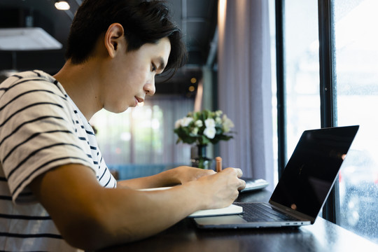 自由职业者在咖啡馆用笔记本电脑辛勤工作的侧视图。