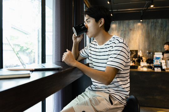 侧视图-年轻的亚洲男子在咖啡馆喝咖啡。