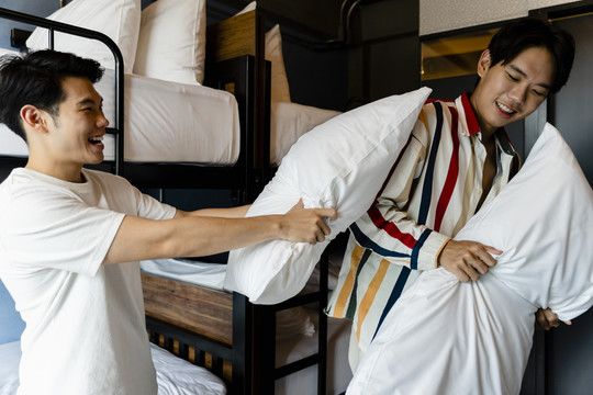 两名亚洲男子在宿舍卧室玩枕头大战。