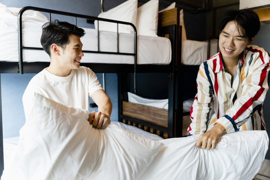两名亚洲男子在宿舍卧室玩枕头大战。