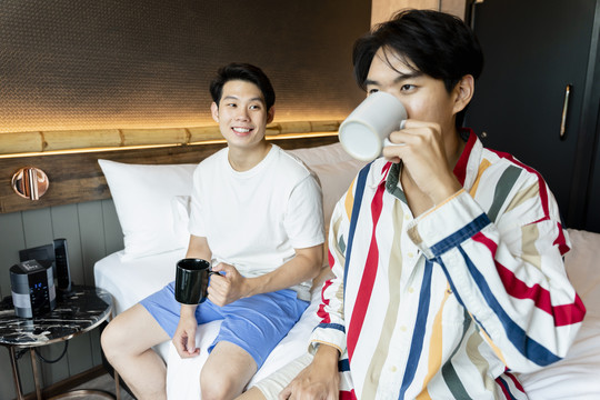 两个亚洲年轻人在卧室里喝咖啡当早餐。