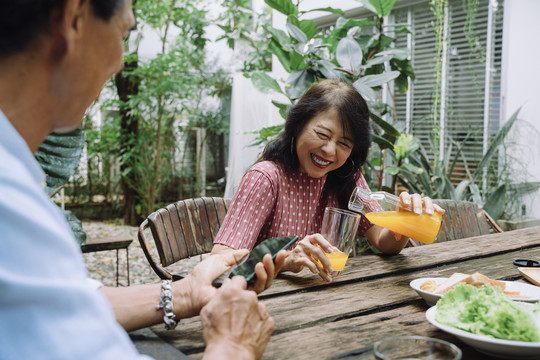一位快乐的亚洲老妇人在后院给丈夫喝橙汁。