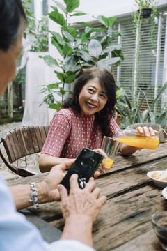 一位快乐的亚洲老妇人在后院给丈夫喝橙汁。