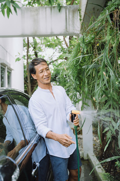 退休的亚洲人在家里的花园里给植物浇水。