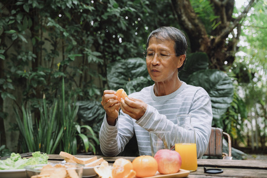 亚洲老人在户外剥橘子皮吃橘子做午餐。