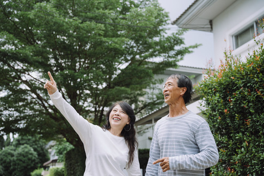 一对亚洲老夫妇一边在公园里散步一边看着飞鸟。