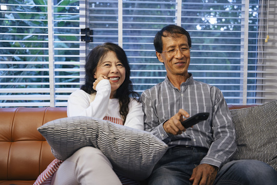 一对亚洲老年夫妇坐在沙发上，一起在家看电视。