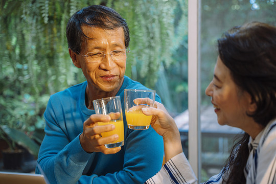 亚洲老年夫妇喜欢在家里一起喝orage果汁。